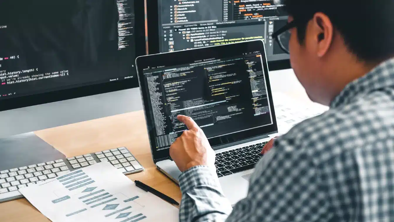 a cybersecurity specialist is working on a laptop in front of two monitors