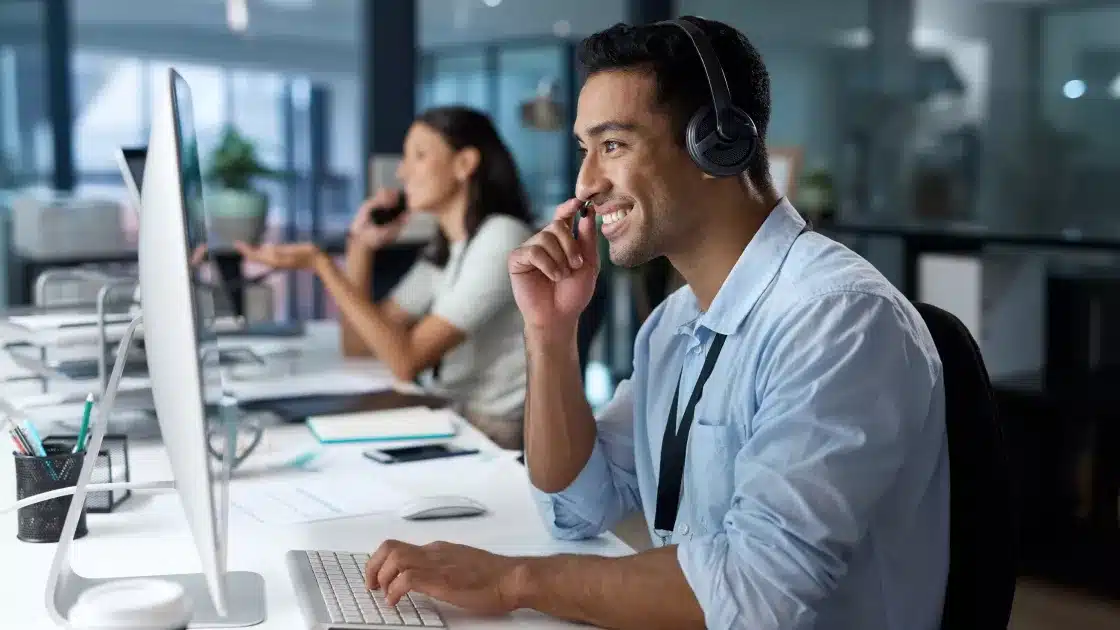 an IT support technician in a headset talking on the phone while sitting at a desk