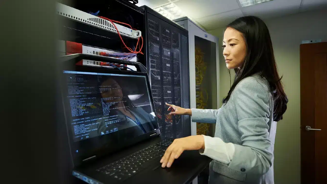 An image of woman looking at hardware servers and checking on her computer