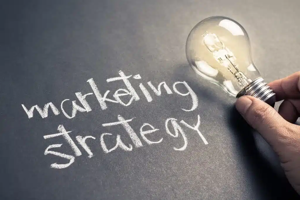 an image of marketing strategy written on chalkboard with hadn holding a lightbulb